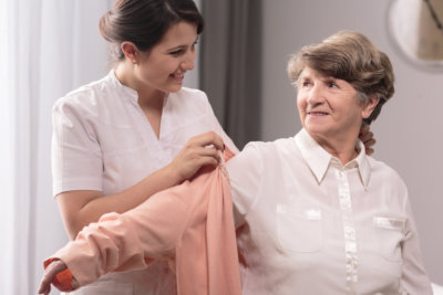 a caregiver assisting senior woman getting dressed